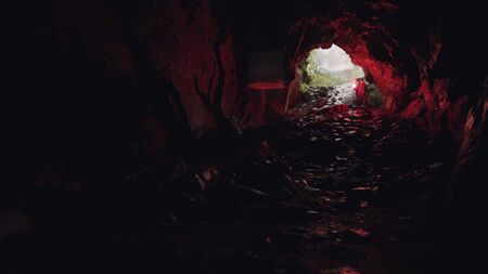 Man walking down inside the cave leaving the entrance behind him, extreme and sport concept. Stock footage. Tourist man in the underground cave with a red signal flare.の写真素材