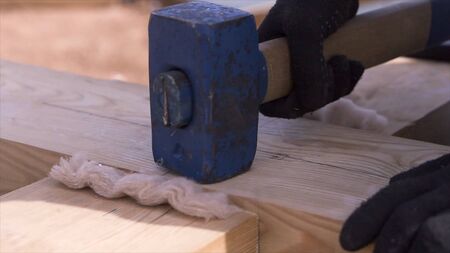 Close up of man hands hitting wooden beam while building the wooden house frame. Carpenter hammering...