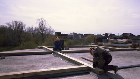 Framing crew rooftop prepairing wooden construction, measuring for better accuracy. Workers standing on the flat roof of the building and measuring wooden beam with a tape.の写真素材
