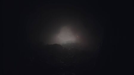 Light passing trough a hole illuminating a mysterious dark cave with a small red signal flare in the fog. Stock footage. View inside of a very old mystical tunnel through mountain rock.の写真素材