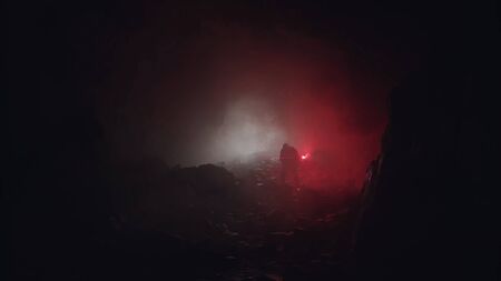 Silhouette of a geologist examining dark cave, holding red signal flare. Stock footage. Scientist man exploring stony old tunnel , nature and paleontology concept.の写真素材