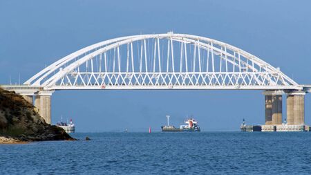 Beautiful seascape with white huge bridge, driving cars, and large ship sailing under the bridge in a summer sunny day. Cargo ships passing behind the bridge, time lapse.の写真素材