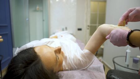 Beautician applying sugaring depilation on arms, hair removal for woman in beauty salon. Young beautiful girl with dark hair gets the procedure for hair removal liquid sugar.の写真素材