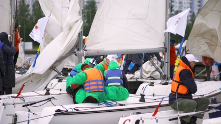People prepare white boats for sailing and competition in windy weather, sport concept. Many people...