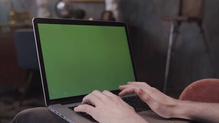 Over the shoulder view of a man sitting at his desk and working on a laptop with Green Screen. Stock Footage. Man using notebook computer with chroma key.の写真素材