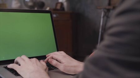 Close up rear view of young businessman hands typing on a laptop keyboard with a blank green...