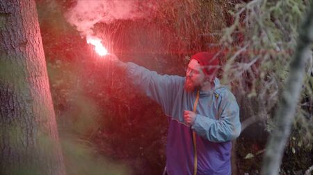 Man with signal stick in nature. Stock footage. Traveler got lost in dense green forest and lit red...