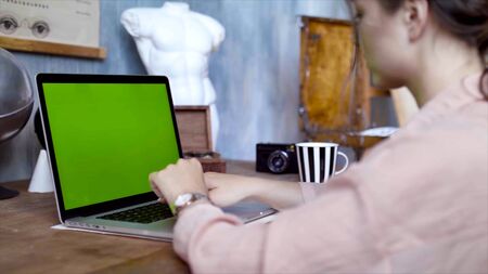 Young woman writing a text on her laptop with green screen. Stock footage. Young female employee engaged in creative work on laptop. Accelerated shootingの写真素材
