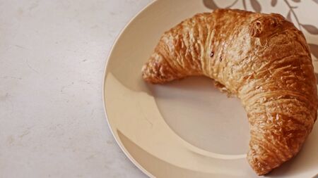 Close up of freshly baked croissant lying on ceramic plate on white table background. Bakery product and food concept.の写真素材