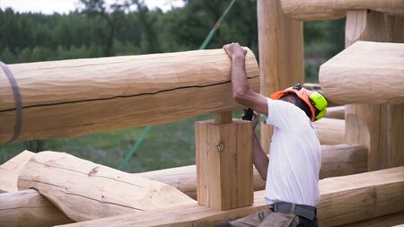 Rear view of a carpenter wearing protective headphones and helmet while installing one of new wooden...