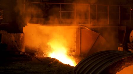 The blast furnace with flowing liquid metal and flying sparkles. Close up of the hot metal production at the factory, heavy industry concept.の写真素材