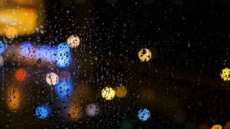 Beautiful defocused bright lights of a big city behind the window with drops of water. Rain drops on...