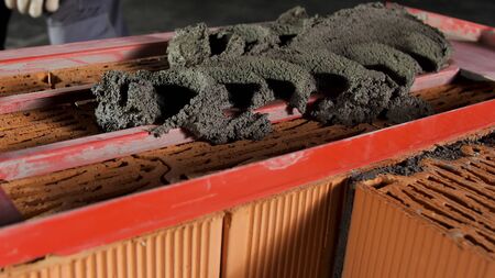 Close up of a worker putting mortar into the wooden frame to make a layer on the brick wall. Stock...