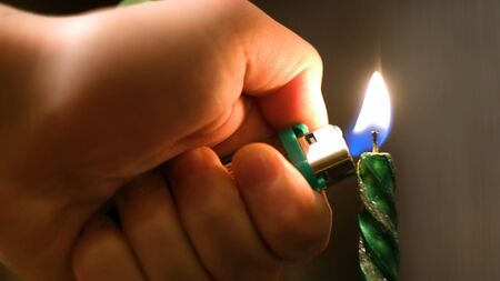 Close-up of man lighting Christmas candle. Concept. Man lights long holiday candle for cozy dinner on background of blurred lightsの写真素材