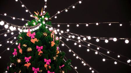 Bottom view of green christmas tree top with garlands and decorative toys on night black sky...