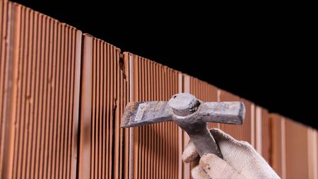 Close up of man hands holding hammer and using it to make an oblong hole on black background. Construction worker demolishing hole at brick wall with a hammer.の写真素材