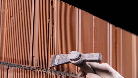 Close up of man hands holding hammer and using it to make an oblong hole on black background. Stock footage. Construction worker demolishing hole at brick wall with a hammer.の写真素材