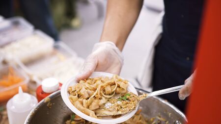 Close up of cook hands putting asian noodles into the disposable plate, asian street food concept....