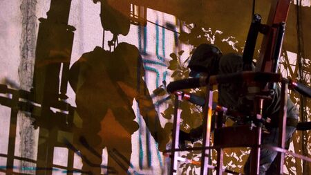 Side view of a graffiti artist drawing symbols with a spray paint on a building wall at night,...