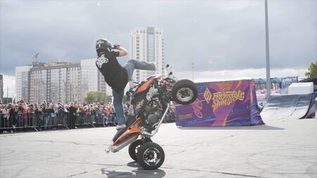 Yekaterinburg, Russia-August, 2019: Man is on ATV performs stunts. Action. Professional Quad bike rider shows tricks on background of crowd of people behind fenceのeditorial素材