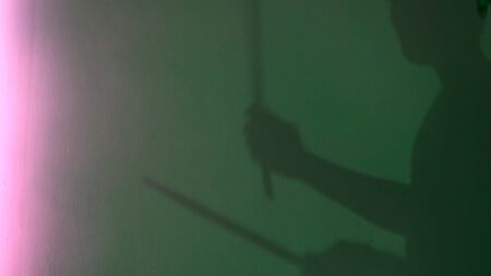Side view of young drummer silhouette with drum stick on green wall background. Male shadow pretending to drum under neon light of lamps, music and art concept.の写真素材