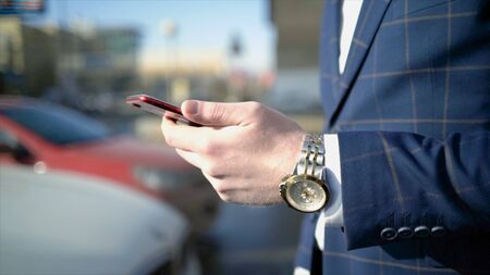 Close-up of businessman pressing car key. Action. Businessman opens car with electronic key and looks at phone. Modern car key to open and start it.の写真素材