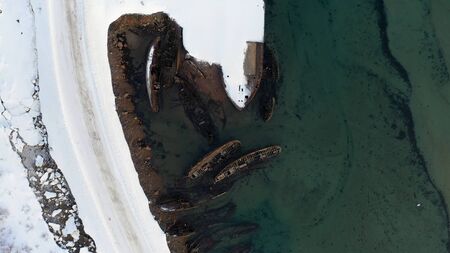 Top view of many old wrecked ships drowned at the sea shore in snowy winter season. Footage. Aerial view of the ruined boats in the cold water near snowy coast.の写真素材