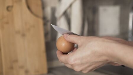 Close up of woman hands breaking the egg with a knife and putting raw white and yolk into the mashed potatoes, cooking concept. Action. Mashed potatoes with eggs in a deep plate in the kitchen.の写真素材