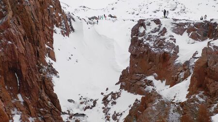Top view of tourists at rocky coast in winter. Footage. Beautiful panorama of tourist hike on snowy...