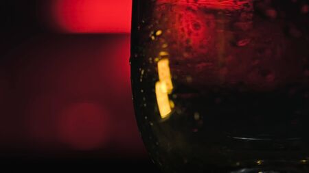 Close-up of ice cubes falling into empty glass. Stock footage. Refreshing ice cubes fall into transparent glass on dark neon background. Cocktail bar.の写真素材