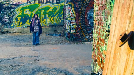 Hippie woman with dreadlocks is walking on street. Stock footage. Beautiful stylish woman with dreadlocks and warm jacket walks along old street with graffiti.の写真素材