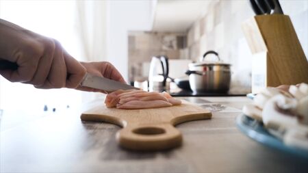 Close-up of slicing chicken breast on board. Action. Slicing raw chicken breast with sharp knife for...
