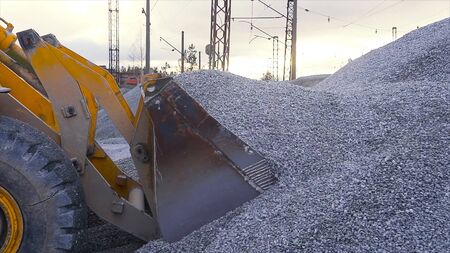 Tractor moves rubble to truck. Stock footage. Excavator-loader rakes rubble from pile at construction site and loads dump truck. Clearing site or mining rubble with heavy transport.の写真素材