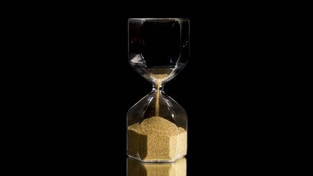 Elegant and stylish bronze transparent sandglass with trickling golden round particles. Stock footage. Sandglass isolated on black background, time, hurry up, last minute, no time concepts.の写真素材