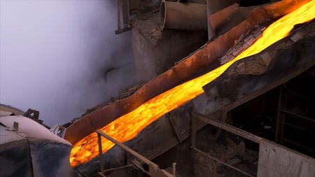 Liquid metal from flowing from blast furnace. Stock footage. Industrial background, melted metal or hot steel on the production line in the hot shop of the factory, professional equipment.の写真素材
