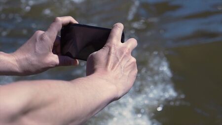Man filming river on phone. Clip. Close-up of hands with phone on background of swirling muddy...