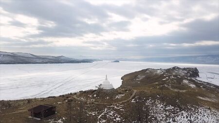 Buddhist stupa on the island of Ogoy on Baikal lake. Clip. Culture and traditions of Siberia, white stupa on frozen water of Baikal on the background, place of divine enlightenment.の写真素材