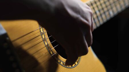 Close-up of man playing guitar. Concept. Professional guitar player moves fingers along strings of...