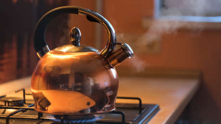 A metal silver teapot on a gas stove in the kitchen at home. Concept. Close up of steel kettle with boiling water, preparation of hot beverage.の写真素材