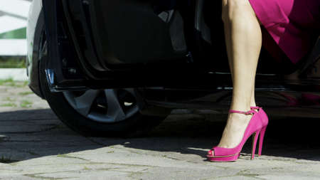 Young lady in pink dress and pink high heeled shoes getting out of the car. Video. Close up of woman with slim sexy legs in high heels getting out of car.の写真素材