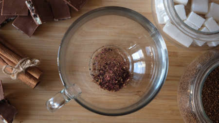 Close up top view of pouring dry red hibiscus tea leaves in a transparent mug. Concept. Process of...
