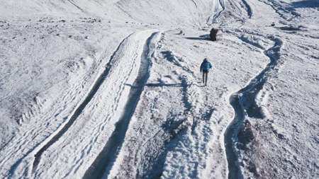 Top view of tourist walking in snowy mountains. Clip. Climber walks along snowy slopes of massive mountain on sunny day. Active recreation in snow-capped mountainsの写真素材