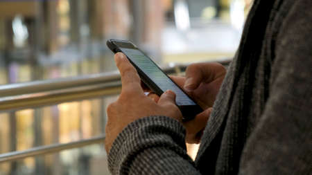 Close up of man hands texting a message on shopping mall background. Media. Male hands using his smartphone for chatting in social net.の写真素材