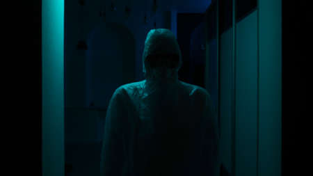 Man in protective suit and mask stands in dark. Stock footage. Man wearing protective coveralls,...