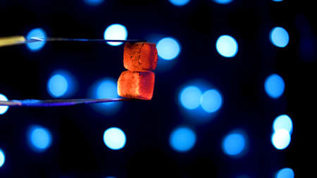 Hot coals for hookah on background of lights. Media. Two hot coals are held with tongs on background of blue lights. Concept of hookahの写真素材