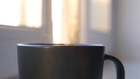 Black mug with steam on background of sunny window. Concept. Close-up of steam coming from black mug...