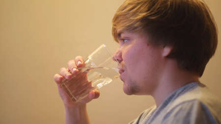 Young dehydrated man drinking filtered mineral clear water. Concept. Side view of thirsty guy...