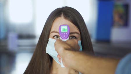 Woman in mask is checked for temperature in mall. Media. Visitors to cinemas and shopping centers are checked for temperature using non-contact thermometerの写真素材