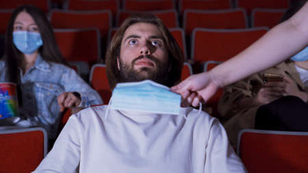 Masked man in movie theater. Media. People in movie theaters must wear protective masks. Man is given medical mask in cinema. Going to cinema during coronavirus pandemicの写真素材