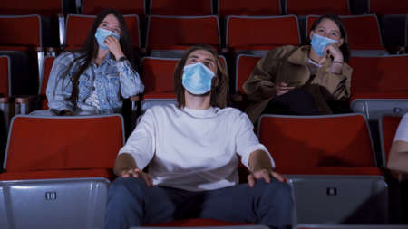 People in masks watch funny movie. Media. People in medical masks sit in movie theater and laugh while watching movie. Opening of cinemas during pandemic coronavirusの写真素材